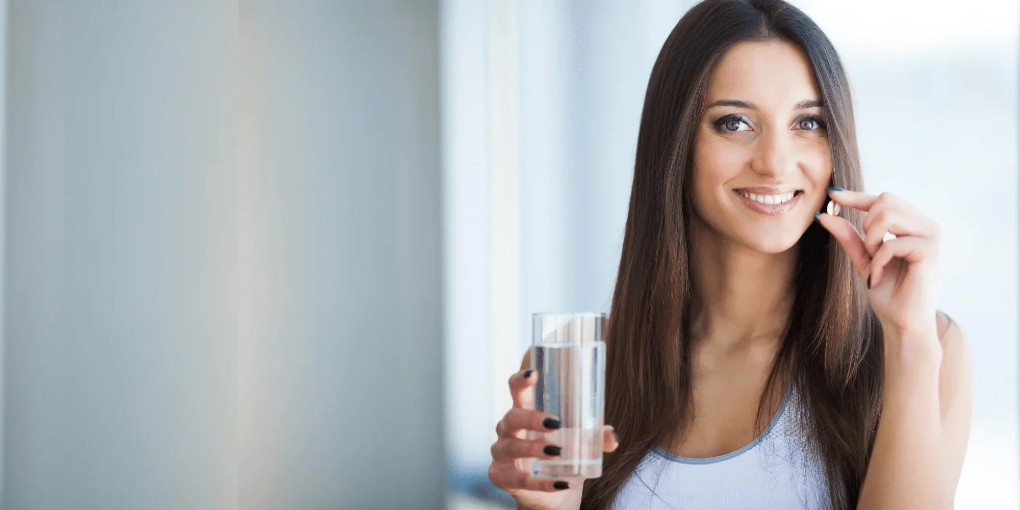 Happy woman holding a Healthogenics supplement capsule with a glass of water